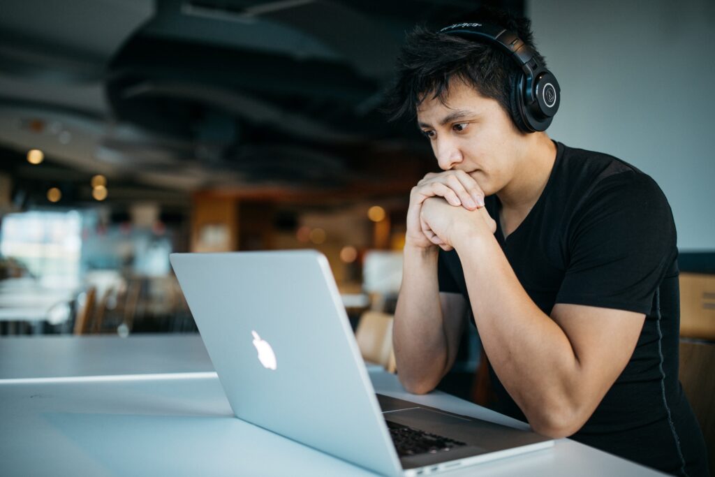 homem com traços asiáticos está concentrado em frente a um computador e usando fones de ouvido over ear. imagem ilustrativa de mentoria de marketing digital